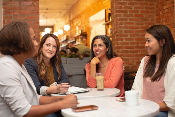 Eine Gruppe von Frauen mit verschiedenen Hautfarben sitzen zusammen an einem Tisch und sind ins Gespräch vertieft.