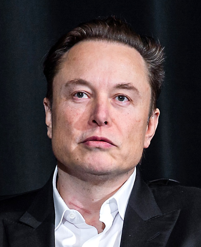 Elon Musk mit kurzen braunen Haaren. Er schaut mit ernstem Blick knapp an der Kamera vorbei.
