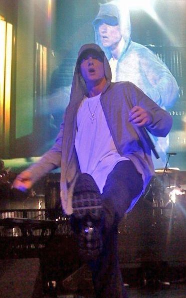 Eminem auf der Bühne. Er macht einen Tanzschritt und trägt eine Kapuzenjacke.