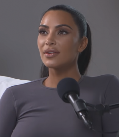 Kim Kardashian mit einem grauen Langarmshirt vor einem Mikrophon. Sie ist stark geschminkt und operiert.