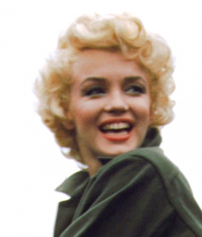 Marilyn Monroe mit kurzen, gelockten blonden Haaren. Sie trägt militärische Kleidung, guckt über die Schulter und lächelt breit.