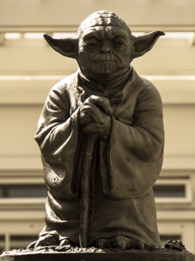 Eine Yoda-Statue mit abstehenden Ohren. Er legt die Hände vor dem Körper zusammen.
