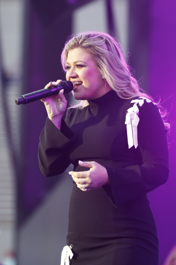 Kelly Clarkson in schwarzem Bühnenoutfit. Sie singt in ein Mikro.