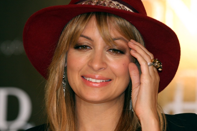 Nicole Richie mit einem großen Hut. Sie schaut in die Kamera und streicht sich die Haare aus dem Gesicht.