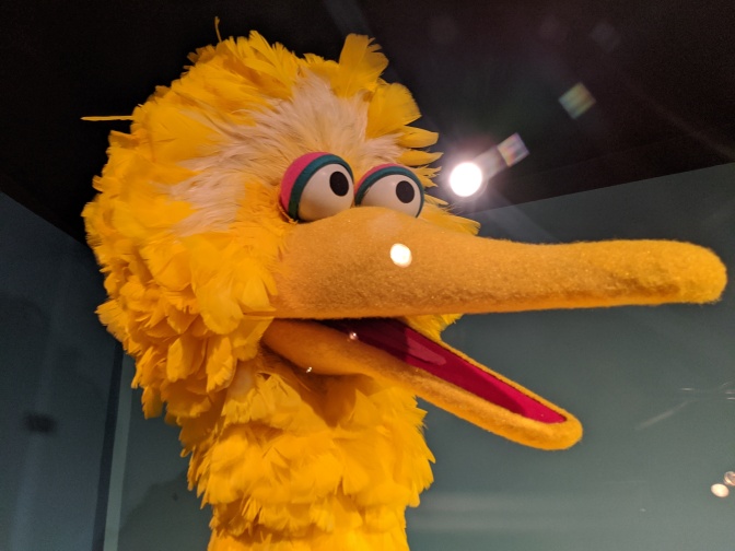 Der Kopf einer großen, gelben Vogelpuppe mit langem, gelbem Schnabel und großen Kulleraugen.