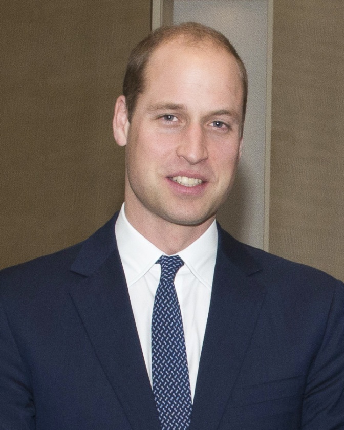 Prinz William mit Stirnglatze in einem dunklen Anzug mit Krawatte