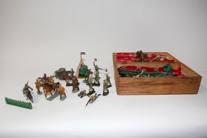 Spielfiguren, zum Beispiel Soldaten mit und ohne Pferd, manche liegen in einer Holzkiste, manche stehen daneben