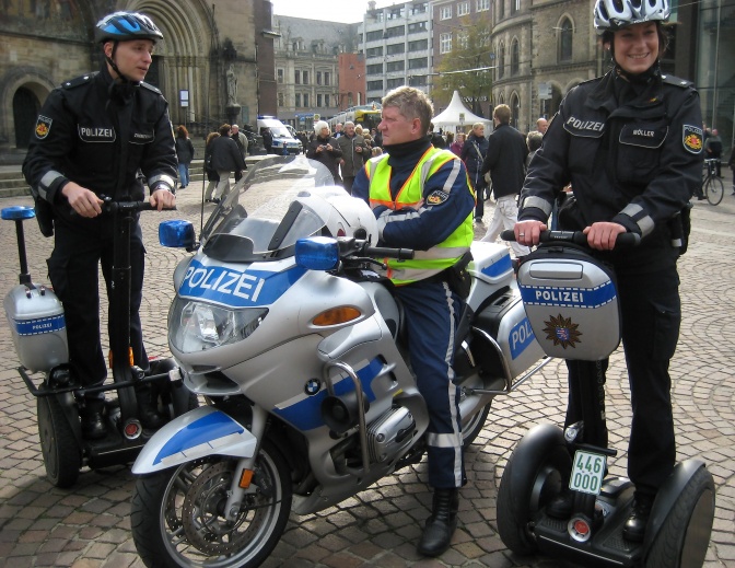 3 Polizisten, einer auf einem Motorrad, 2 auf Segways