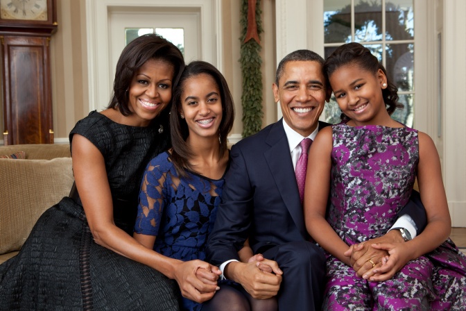 Michelle und Barack Obama mit ihren beiden Töchtern, alle lächeln und umarmen sich.