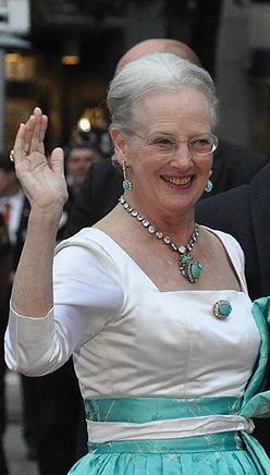 Margrethe von Dänemark winkt und lächelt. Sie trägt eine große Robe und ein Diadem auf dem Kopf.