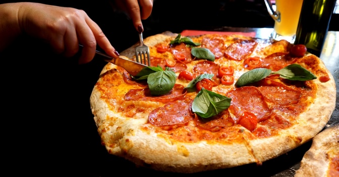 Eine große Pizza wird mit Messer und Gabel zerteilt