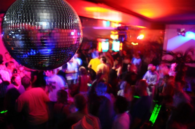 Gäste auf einer Party tanzen unter einer Disko-Kugel