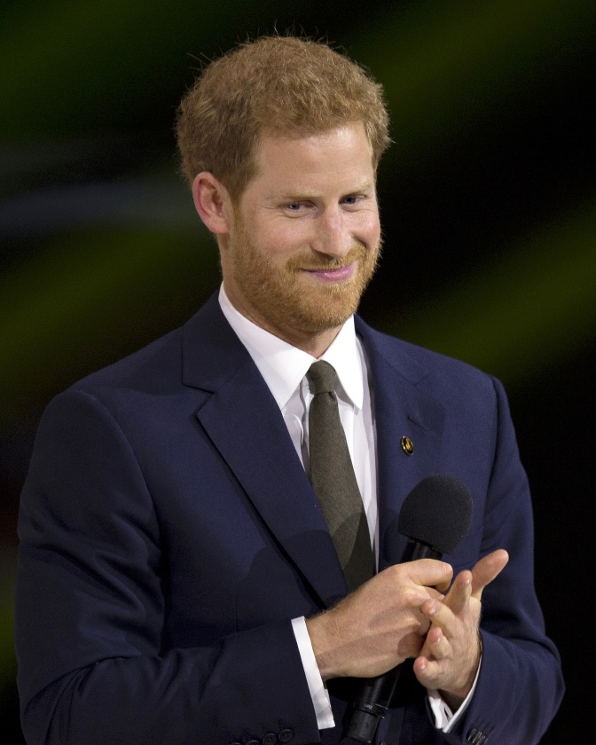 Prinz Harry in Anzug und Krawatte. Er lächelt und legt seine Hände ineinander.