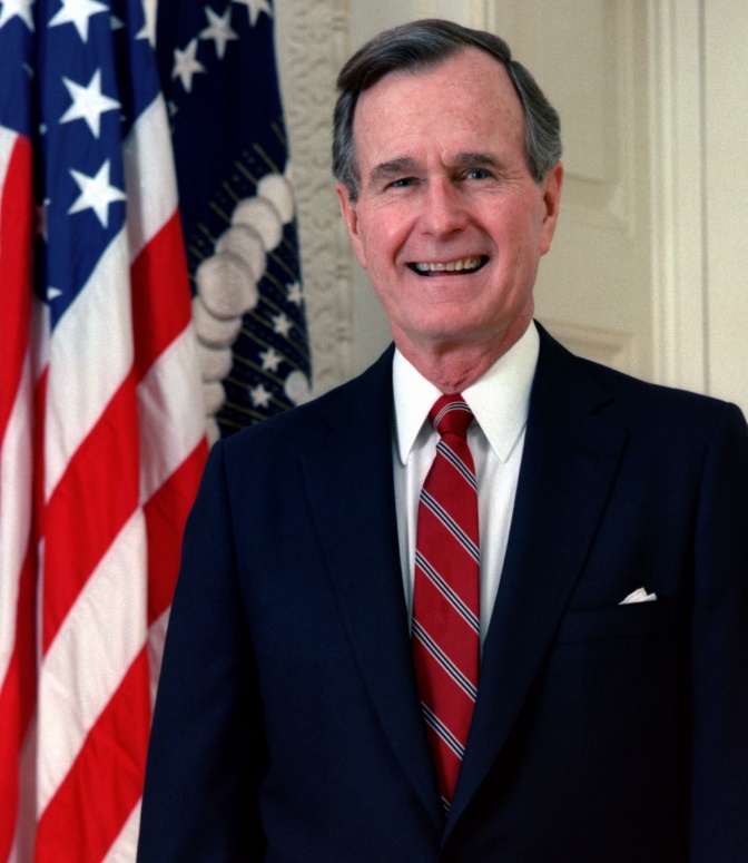 George H. W. Bush in Anzug und Krawatte vor der amerikanischen Flagge
