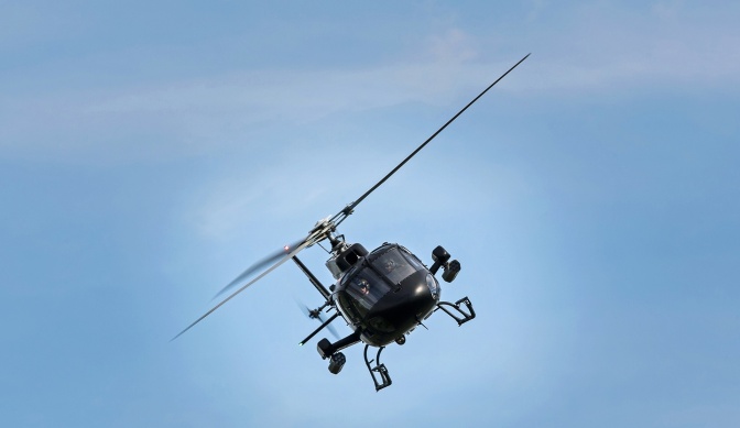 Ein Hubschrauber fliegt schräg durch wolkenlosen, blauen Himmel