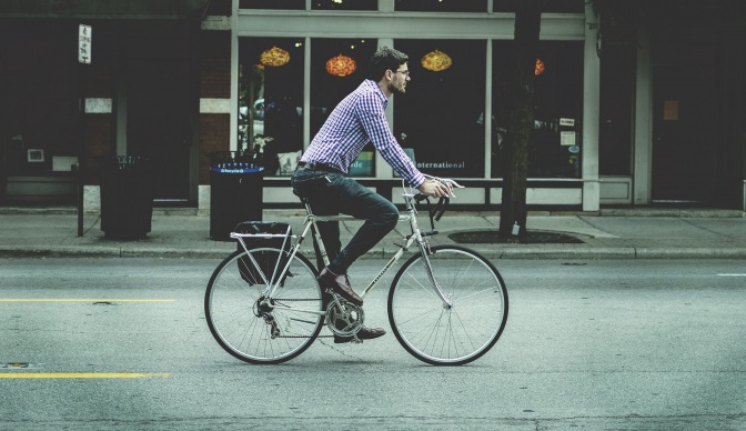 Ein Mann auf einem Fahrrad fährt an einer Laden-Passage vorbei. Er trägt ein kariertes Hemd.