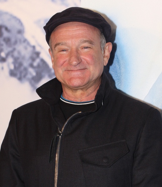 Robin Williams lächelt. Er trägt eine schwarze Schiebermütze und eine schwarze Jacke mit Reißverschluss.