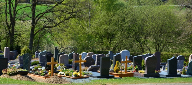 Grabsteine und Holzkreuze in Reihen neben- und hintereinander auf einem Friedhof