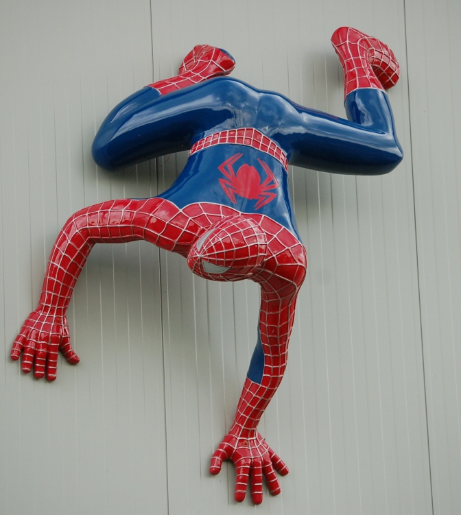 Spider-Man in seinem Superhelden-Anzug. Er klettert kopfüber an einer Hauswand.