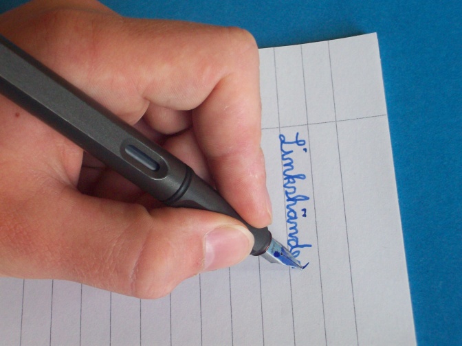 Jemand schreibt mit der linken Hand mit einem Füller das Wort Linkshänder.