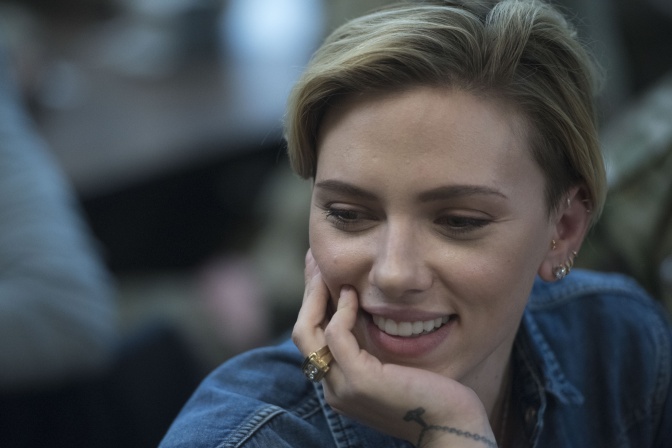 Scarlett Johansson stützt das Kinn in die Hand und lächelt. Sie trägt eine Jeansjacke.