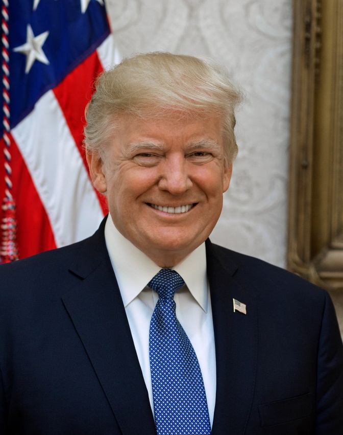 Donald Trump steht lächelnd vor der amerikanischen Flagge. Er trägt Anzug und Krawatte.