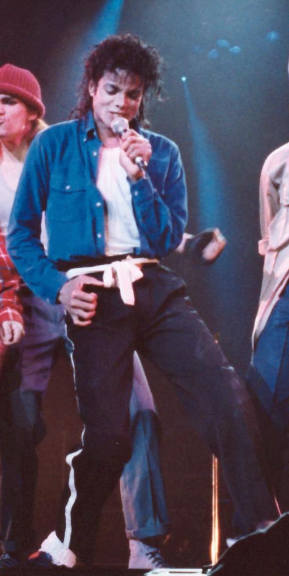 Michael Jackson in einem Bühnenoutfit. Er singt in ein Mikrophon.