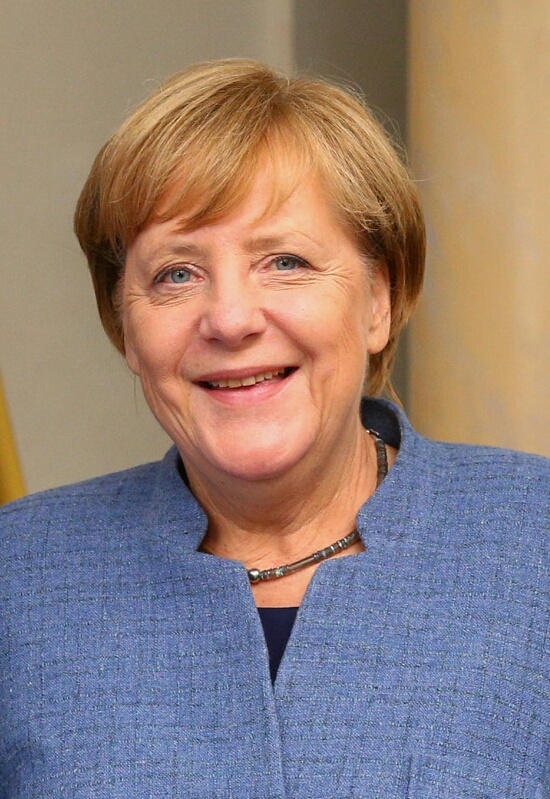 Angela Merkel lächelt breit. Sie trägt ein hellblaues Oberteil.