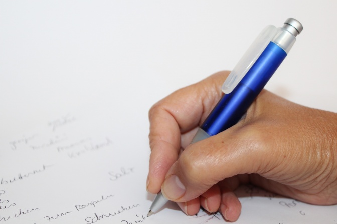 Eine Frau schreibt mit einem Kugelschreiber eine Einkaufsliste auf liniertes Papier.