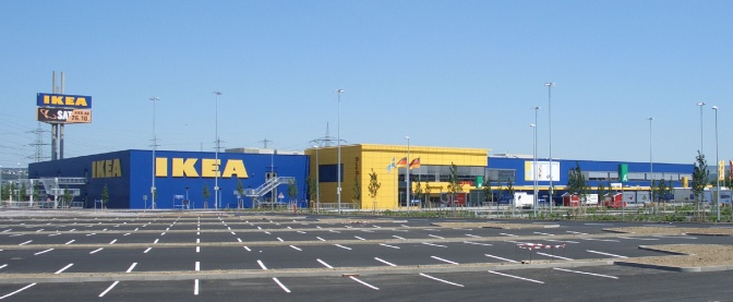 Ein großer, leerer Parkplatz vor einer Ikeafiliale, dahinter das Möbelhaus in den schwedischen Farben gelb und blau.