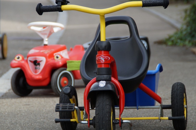Ein Dreirad für Kinder, im Hintergrund ein Bobby Car.