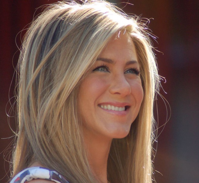 Jennifer Aniston mit langen, geglätteten blonden Haaren mit Strähnchen. Sie lächelt.