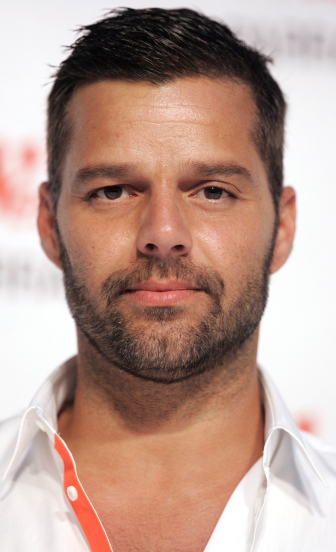 Ricky Martin mit einem leichten Bart und in weißem Hemd. Er schaut ernst in die Kamera.
