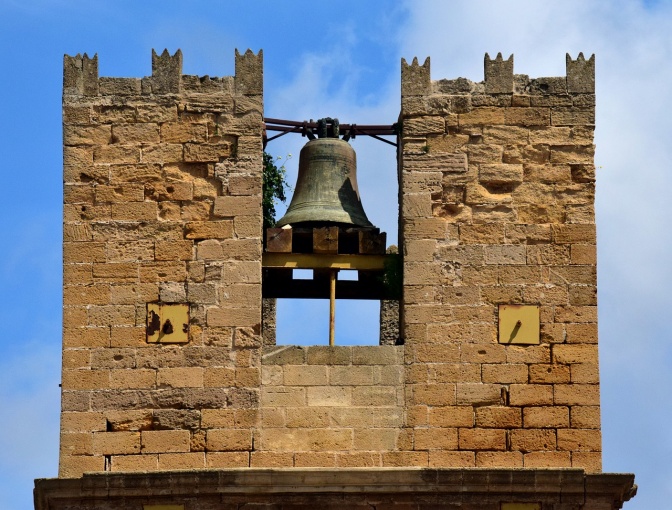 Ein gemauerter Glockenturm mit einer frei hängenden Glocke.