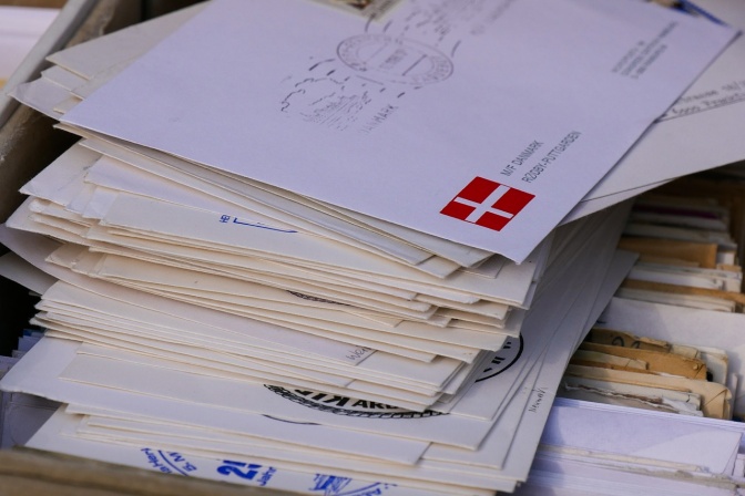 Ein Stapel mit Briefumschlägen. Auf dem obersten sind eine handgeschriebene Adresse und eine kleine dänische Flagge zu sehen.