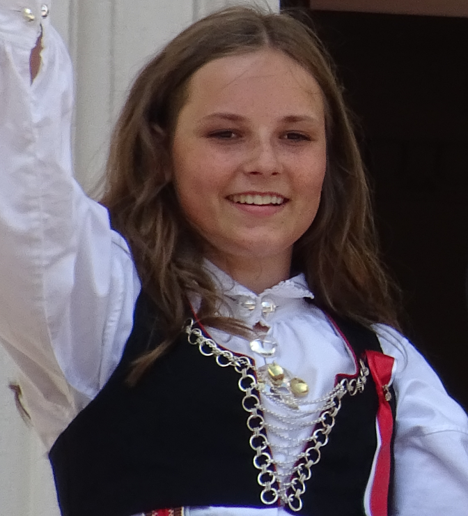 Ingrid Alexandra von Norwegen in norwegischer Tracht. Sie winkt und lächelt.