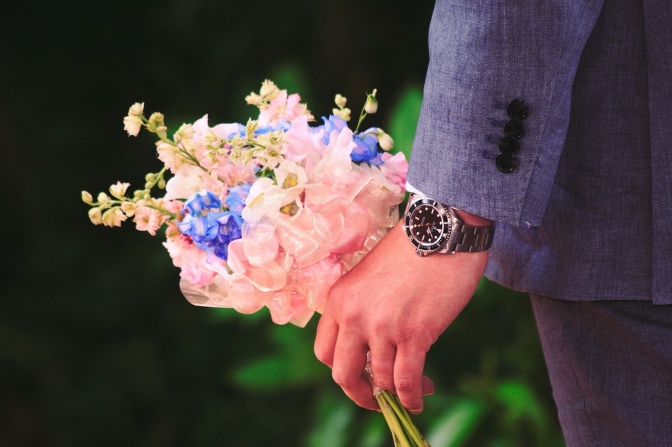 Ein Mann in Anzug hält einen Blumenstrauß in der Hand. Er trägt eine Armbanduhr.