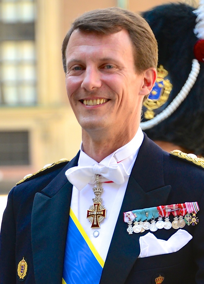 Prinz Joachim von Dänemark steht lächelnd vor einem Schloss. Er trägt eine mit zahlreichen Orden dekorierte Uniform.