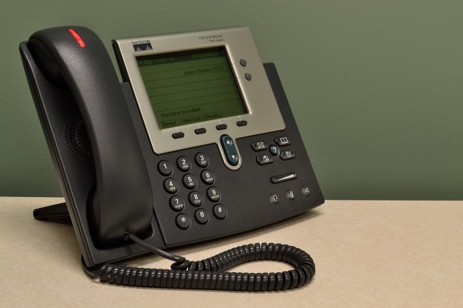 Ein Festnetztelefon mit Schnur. Am Hörer sieht man ein rotes Licht, das signalisiert, ob ein Anruf auf dem Anrufbeantworter hinterlassen wurde.