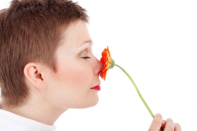 Eine kurzhaarige Frau riecht an einer Blume.