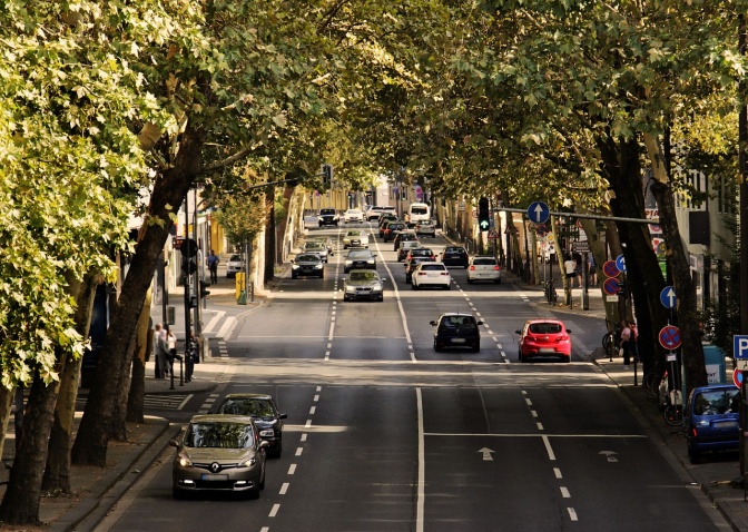 Autos fahren in beide Richtungen über eine vierspurige Straße. Am Straßenrand stehen verschiedene Verkehrsschilder.