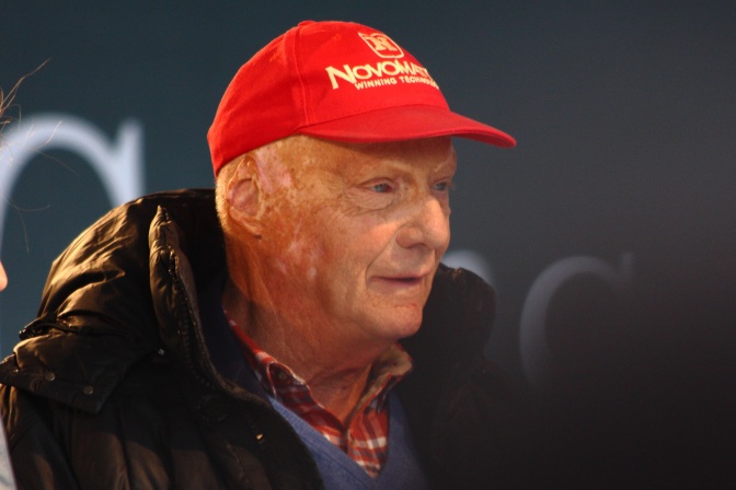 Niki Lauda mit einer roten Schirmmütze und einer schwarzen Daunenjacke. Er ist im Profil fotografiert.
