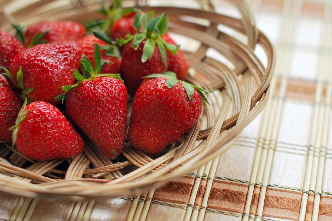 Ein geflochtenes Körbchen mit Erdbeeren steht auf einer karierten Tischdecke.