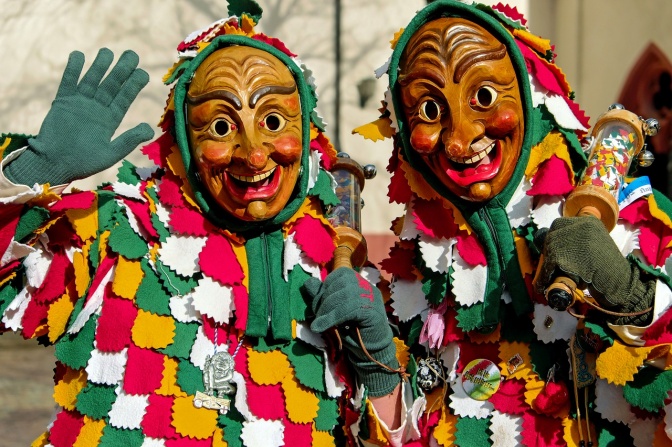 2 Narren in Kostüm mit Masken und Kitteln aus vielen einzelnen, farbigen quadratischen Stoffstücken.