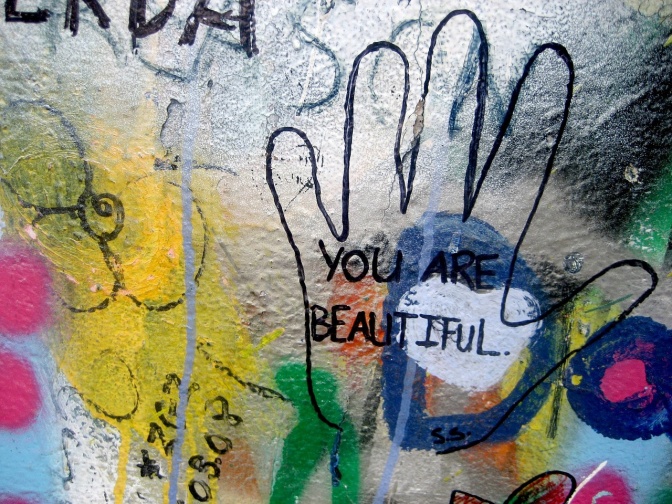 Eine bemalte Wand in vielen Farben. Unter anderem der Umriss einer Hand, in der steht: You are beautiful.
