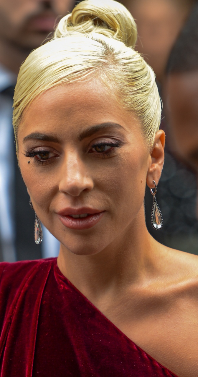Lady Gaga in einem asymmetrischen dunkelroten Samtkleid und mit hochgesteckten, hellblonden Haaren