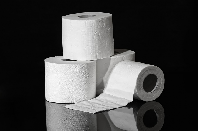 4 Rollen Toilettenpapier. Eine davon liegt seitlich und ist eine Blatt lang abgerollt.
