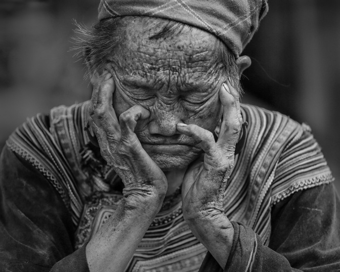 Eine alte asiatische Frau hat das Gesicht in beide Hände gestützt und schläft. Das Bild ist ein schwarz-weiß-Foto.