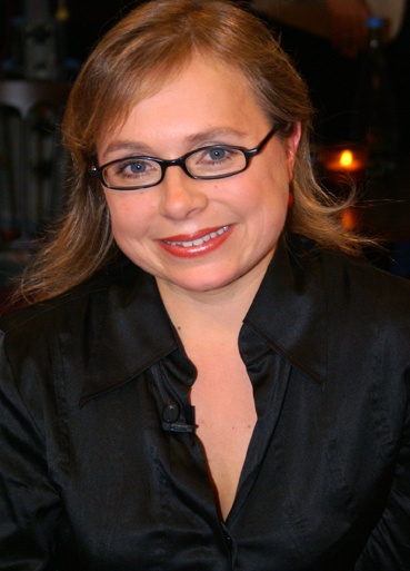 Christine Urspruch mit schwarzer Kleidung und schwarzer Brille. Sie hat halblanges, glattes Haar und lächelt in die Kamera.