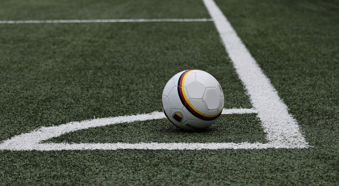 Ein Ball liegt auf der Ecke eines Fußballfeldes. Um den Ball herum sieht man weiße Markierungen.